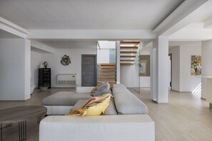 A spacious living area with a modern sofa, a wooden staircase, and a radiator.
