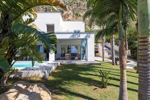 Una casa moderna con piscina, rodeada de plantas tropicales y palmeras.