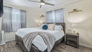 Ein Schlafzimmer mit einem hölzernen Bett, einem Deckenventilator, einem Nachttisch mit Lampe und einer kleinen Uhr.
