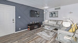 Ein modernes Wohnzimmer mit grauem Sofa, einem Flachbildfernseher und einem dekorativen Spiegel.