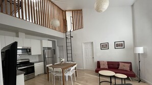 A modern kitchen with white cabinets, a stainless steel refrigerator, and a dining area with a wooden table and white chairs. - Loft 654B two blocks from BART (Richmond)