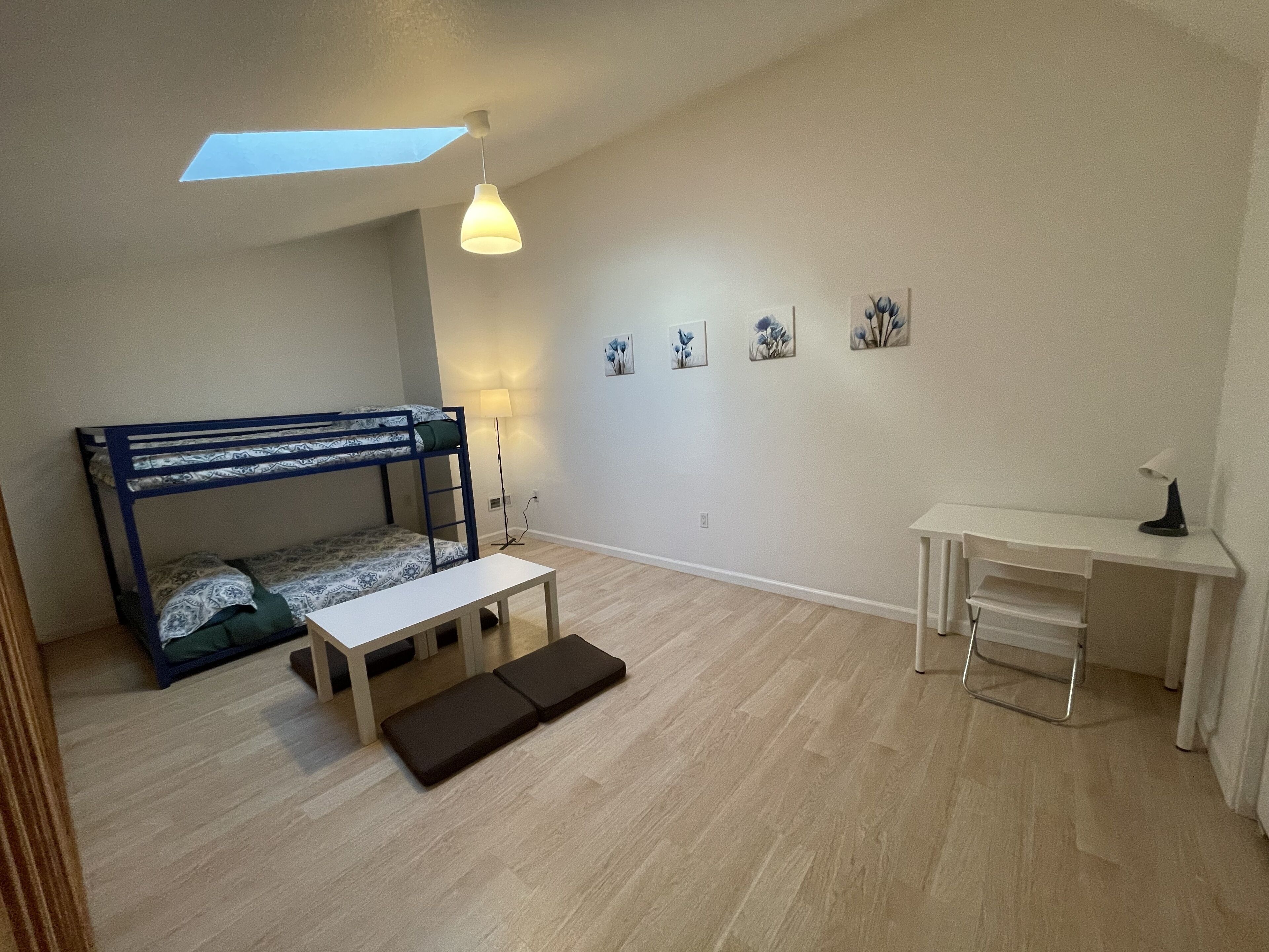 A compact room with a bunk bed, a desk, a lamp, and a skylight.
