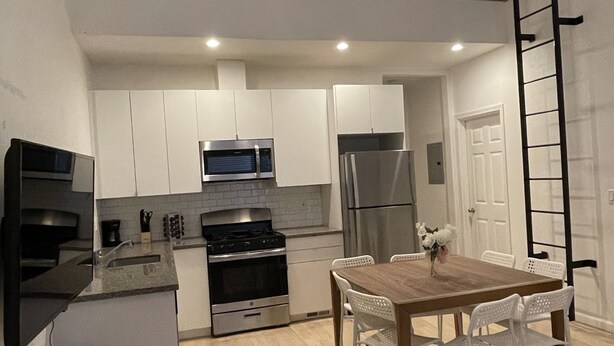 A modern kitchen with white cabinets, stainless steel appliances, and a wooden dining table with white chairs. - Loft 654B two blocks from BART (Richmond)