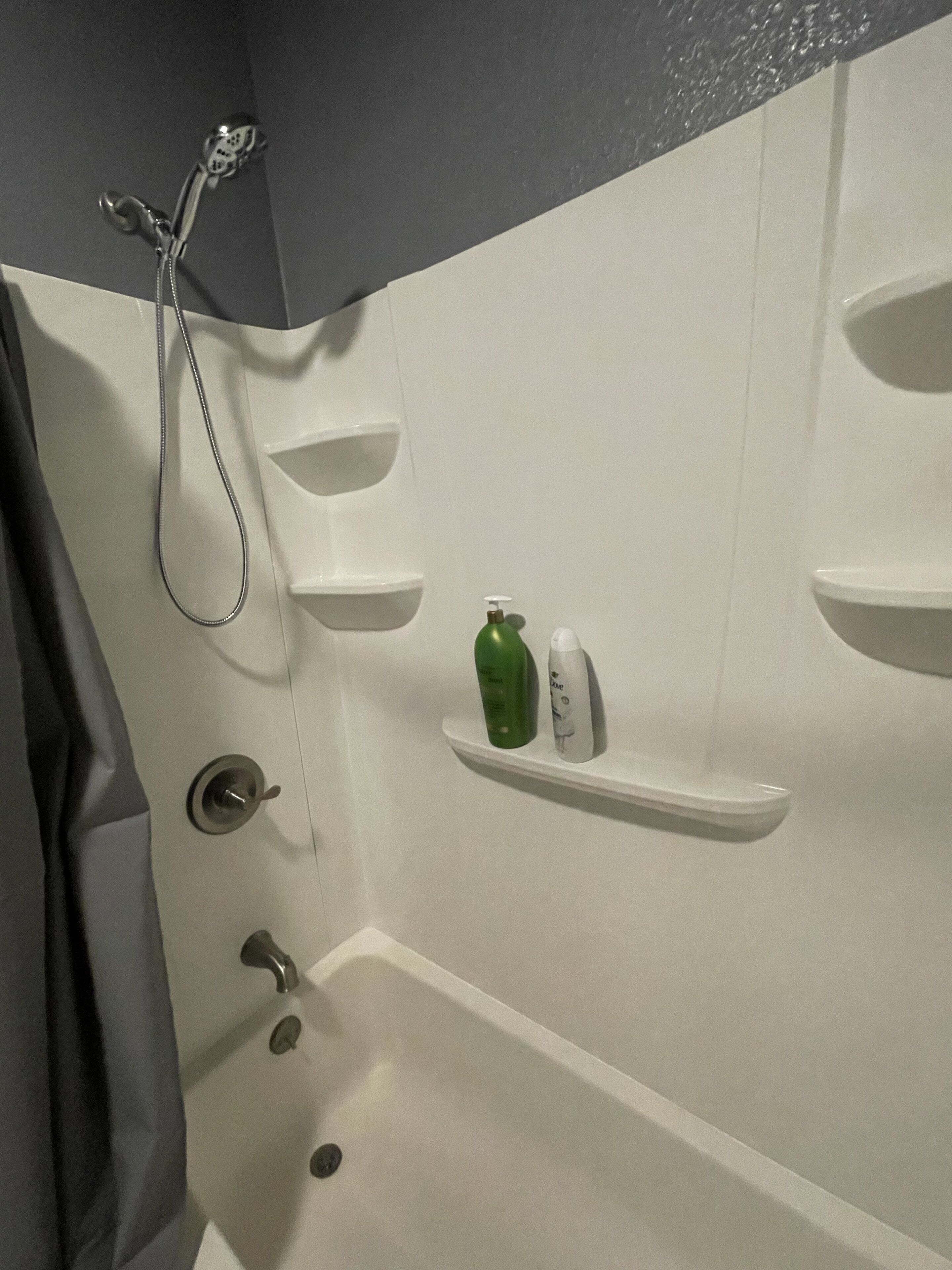 A bathroom with a bathtub, a shower, and a shelf with toiletries.