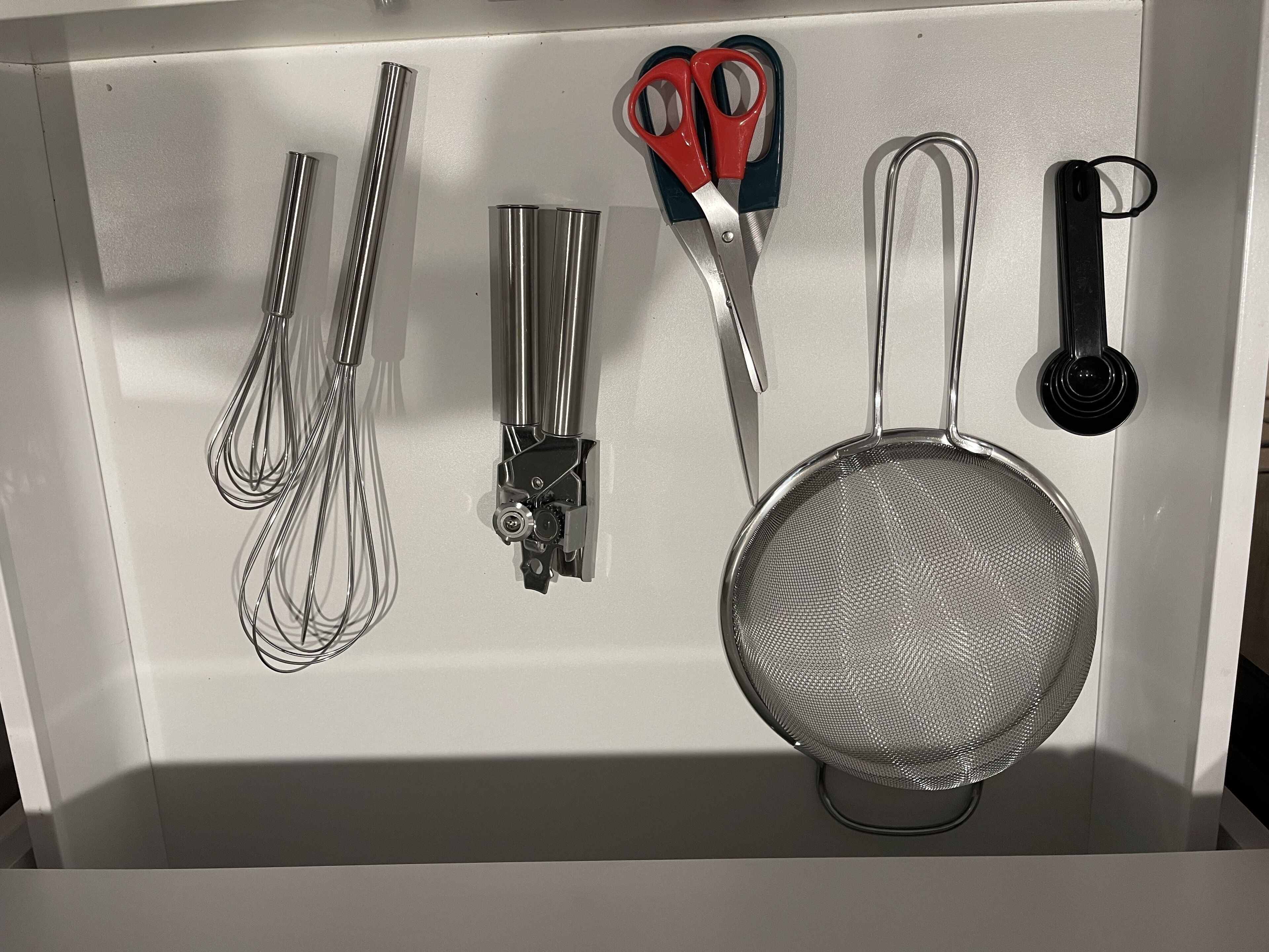 Ett kök med köksredskap i rostfritt stål, inklusive vispar, en sil och ett par saxar.
