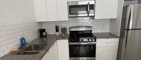 A modern kitchen with white cabinets, a stainless steel refrigerator, a microwave, and a stove.