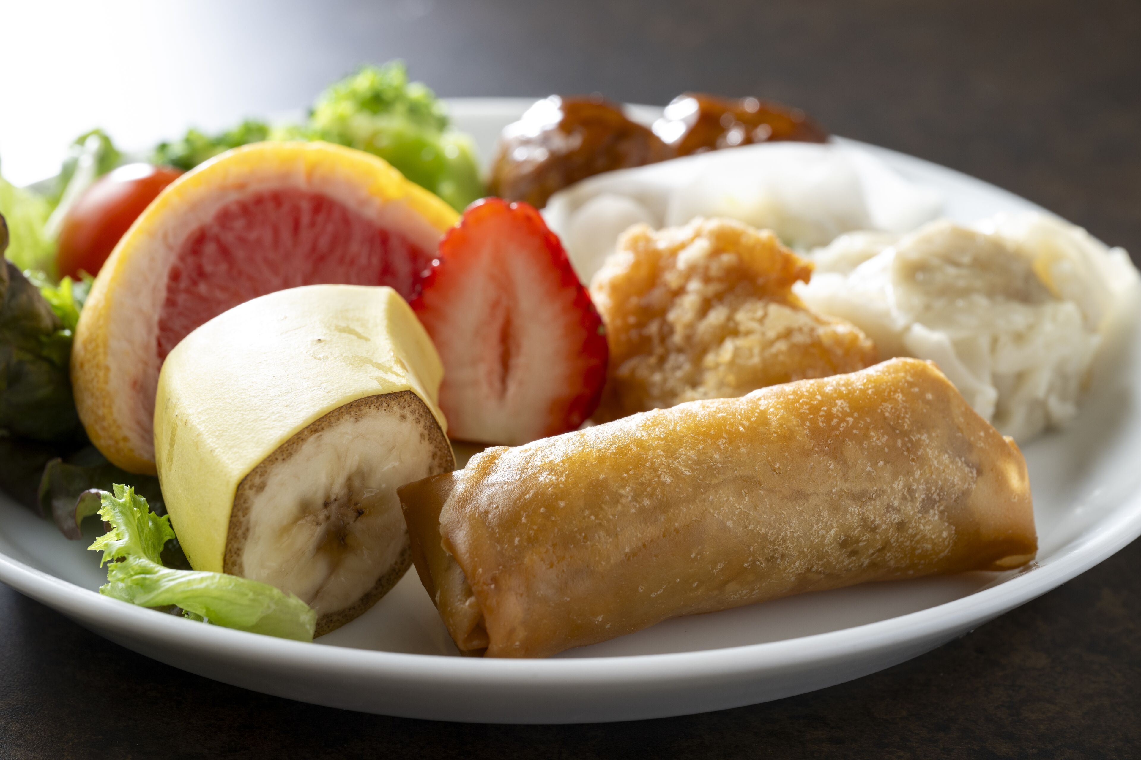 Une assiette contenant divers aliments, notamment une banane, une fraise, un pamplemousse et un plat frit.