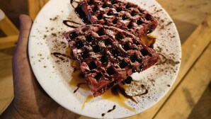 Una mano sosteniendo un plato de gofres y almíbar.