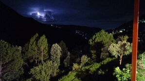 Vista nocturna de una zona montañosa con una edificación iluminada en primer plano y una ciudad distante.