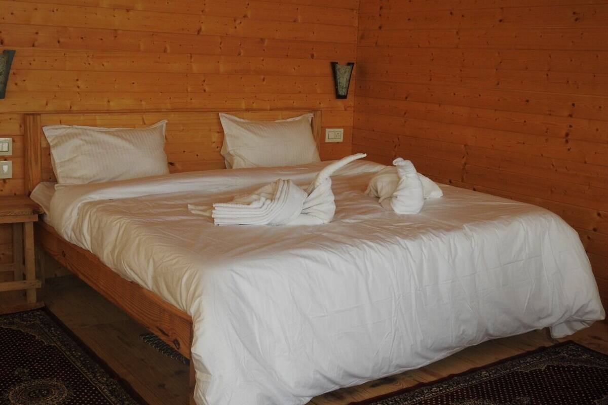 A wooden-paneled room with a bed, pillows, a nightstand, and a wall-mounted light fixture.