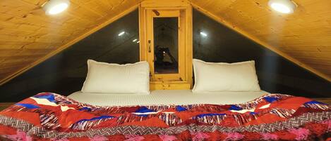 Un dormitorio acogedor en el ático, con techo inclinado, una cama grande con una manta colorida y un cabecero de madera.