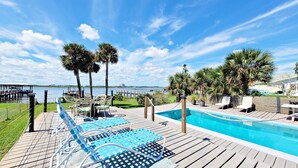 Eine Holzterrasse mit Pool, Liegestühlen und Palmen.
