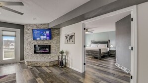 A modern hotel room with a stone accent wall, a flat-screen TV, a bed with a wooden headboard, and a view of the outdoors. - Sparrow's Nest - Stay at the lake, walk to Noah's Ark! (Wisconsin Dells)