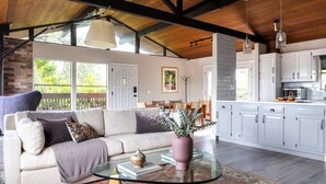 A spacious living area with a sofa, a glass coffee table, and a view of a kitchen with white cabinets.