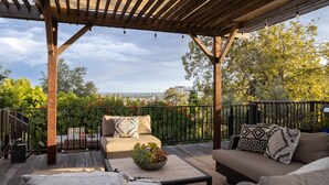 A covered outdoor seating area with a wooden pergola, black metal railing, and a view of the cityscape.