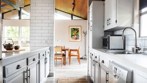 A modern kitchen with white cabinetry, a dining area with wooden chairs, and a large window providing natural light.
