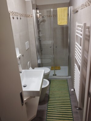 Ein modernes Badezimmer mit einer in Glas abgeschlossenen Dusche, einem weißen Waschbecken und einer Toilette.