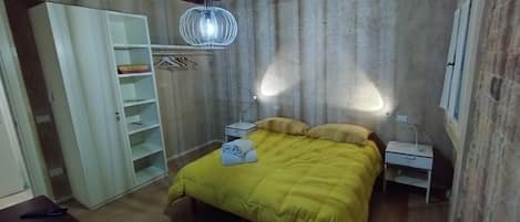 A bedroom with a bed, a wardrobe, a bedside table, and a hanging light fixture.