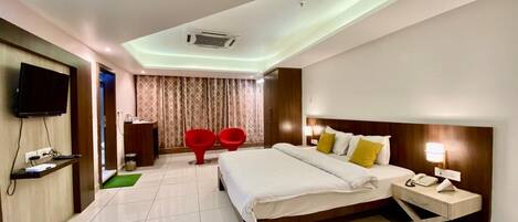 A hotel room with a bed, bedside table, TV, and a small desk with a chair.