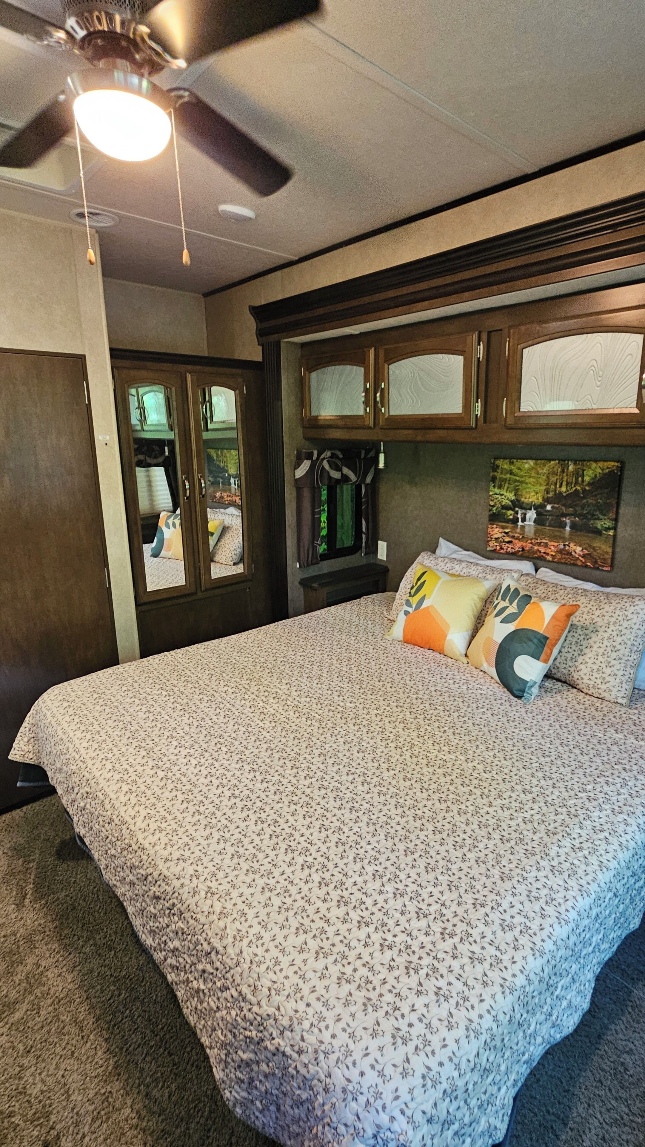 A bedroom with a bed, a ceiling fan, a window with curtains, and a wall-mounted TV.