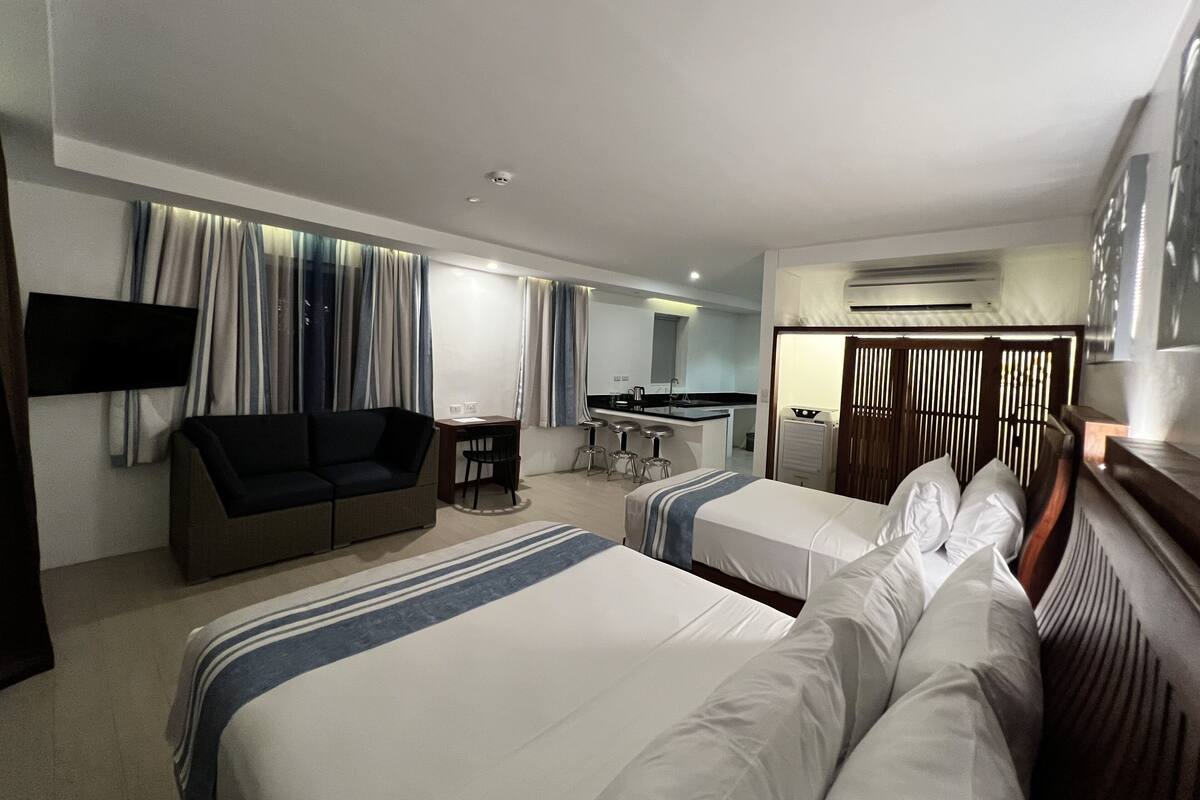 Ein Hotelzimmer mit zwei Betten, einer Couch, einem Schreibtisch und einer Küchenzeile.