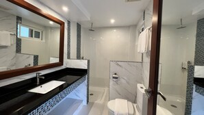 Un baño moderno con encimera negra, lavabo blanco, un espejo grande, cabina de ducha con mampara de vidrio y un inodoro.