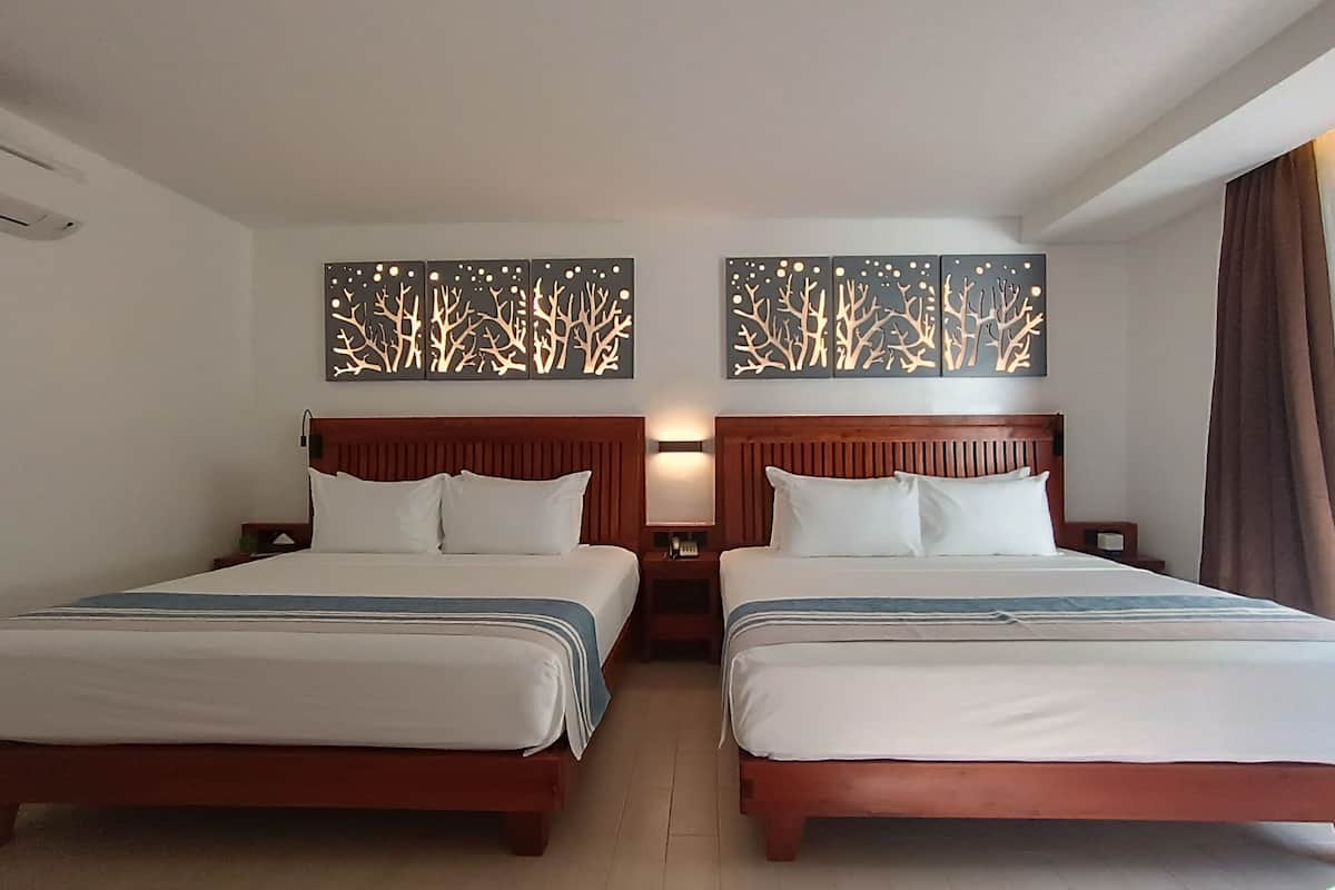 Ein Hotelzimmer mit zwei Betten, einem hölzernen Kopfteil, einem Nachttisch und Wandbildern.