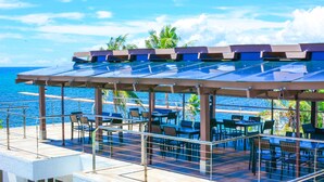 Un área de comedor al aire libre con mesas y sillas, con vista a un cuerpo de agua.