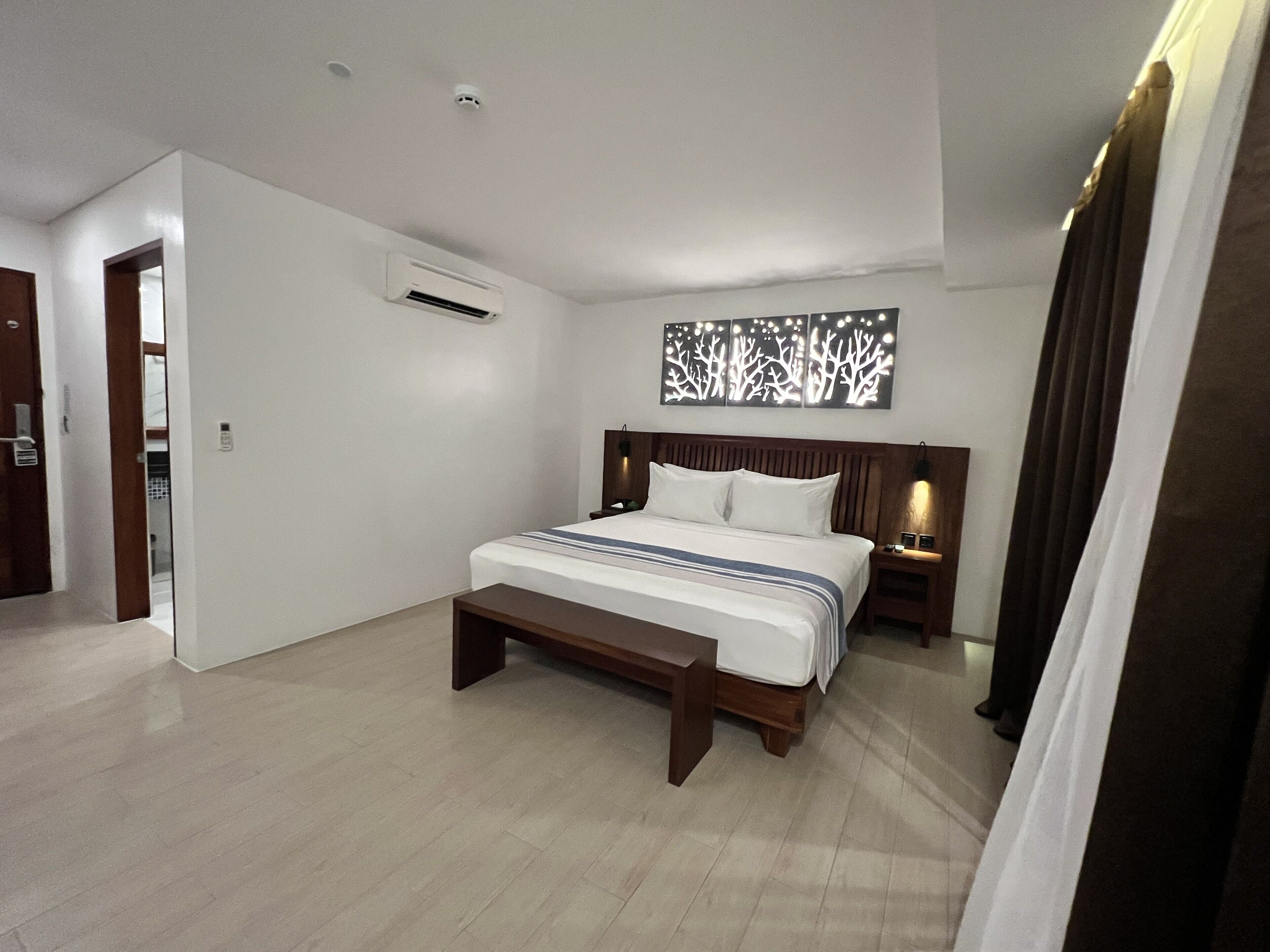Une chambre moderne avec un grand lit, une tête de lit en bois, des tables de chevet et un climatiseur fixé au mur.