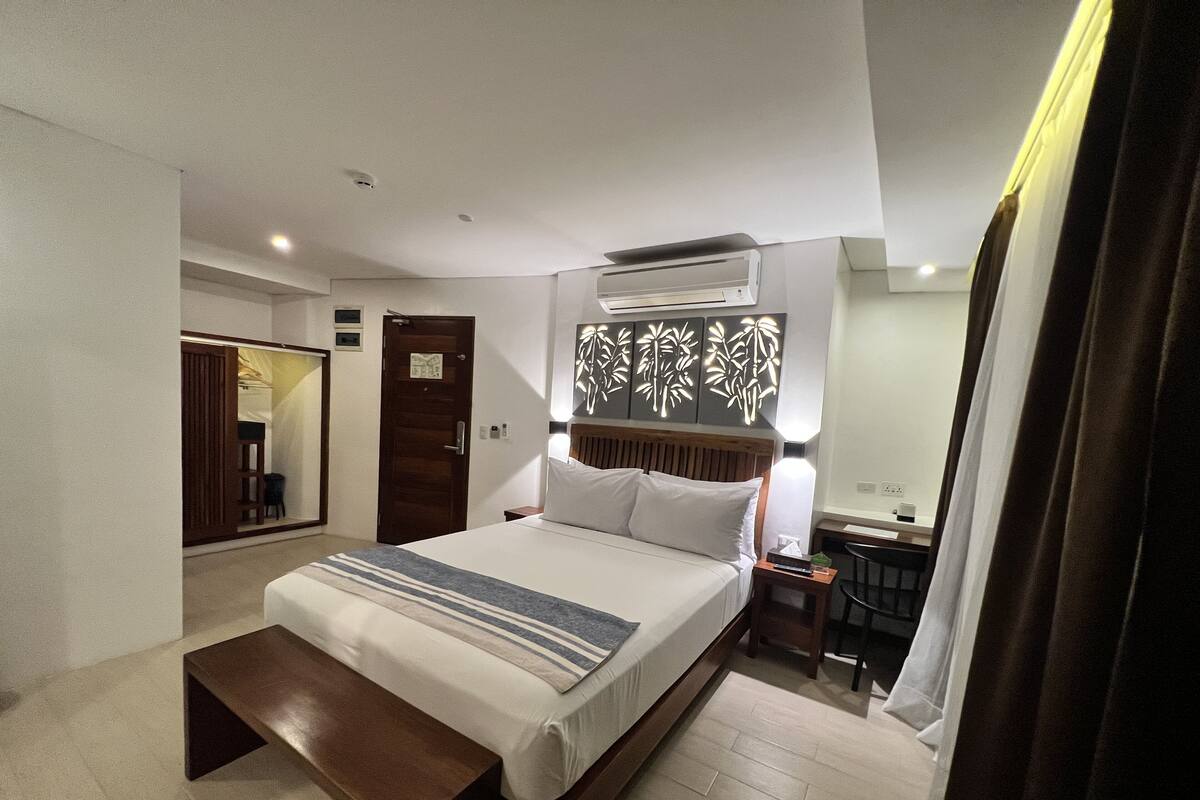 Ein Hotelzimmer mit einem Bett, einem Nachttisch, einer Lampe und einem Schreibtisch mit Stuhl.