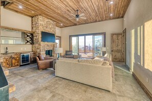 Un amplio espacio de sala con chimenea de piedra, un sofá grande y un televisor montado en la pared.