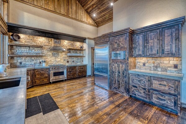 Una cocina con paredes de piedra, armarios de madera y un refrigerador de acero inoxidable.