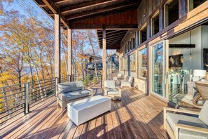 A wooden deck with outdoor seating, large windows, and a view of trees and buildings. - Greystone Lodge - Hot tub & mountain views (Mineral Bluff)