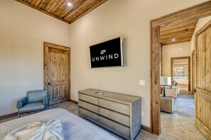 A bedroom with a bed, a dresser, a chair, and a television displaying 'UNWIND'. - Greystone Lodge - Hot tub & mountain views (Mineral Bluff)