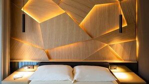 A modern hotel room with a geometric wooden wall design, a bed with white linens, and two bedside tables with lamps.