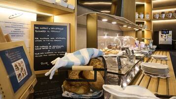 Un comptoir de boulangerie avec du pain, un tableau noir affichant le menu et une machine à café.