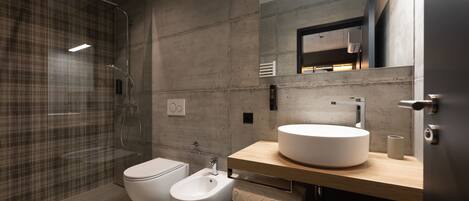 A modern bathroom with a glass-enclosed shower, a toilet, a bidet, and a sink with a mirror above it.
