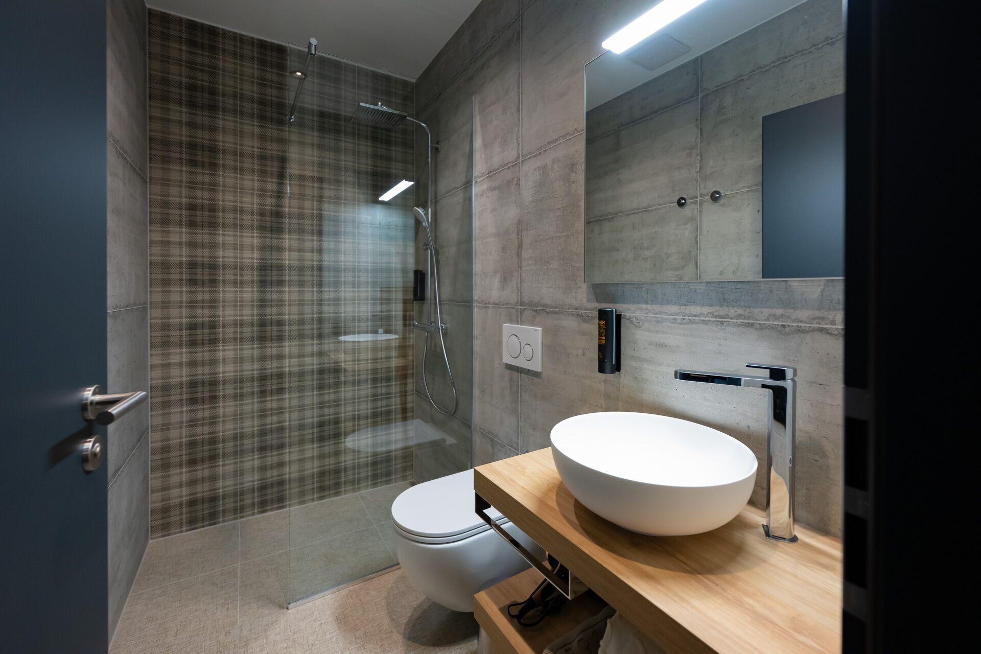 Un baño moderno con ducha de vidrio, inodoro blanco y un lavabo redondo grande con espejo arriba.