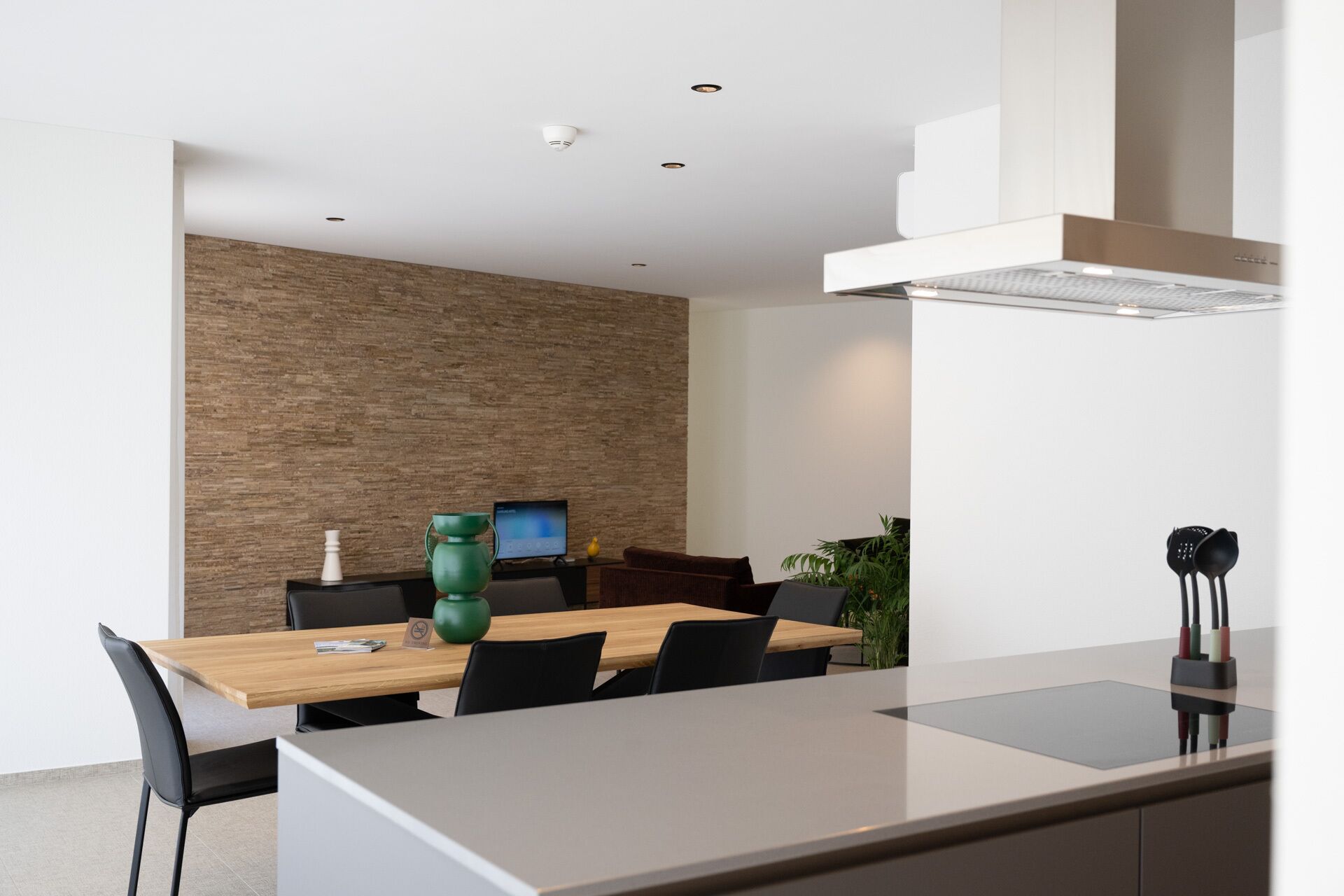 A modern dining area with a wooden table, black chairs, a green vase, and a laptop on the table.