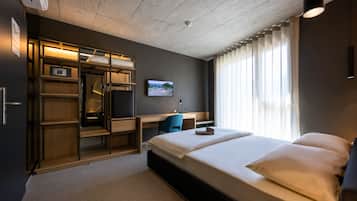 A modern hotel room with a bed, a desk, a chair, and a wardrobe.