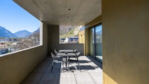 A balcony with a table and chairs, overlooking a mountainous landscape.