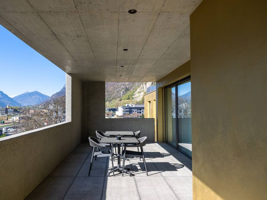 A balcony with a table and chairs, overlooking a mountainous landscape.