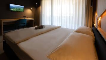 A hotel room with a large bed, a desk, a chair, and a TV on the wall.