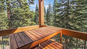 A wooden deck with a bench, surrounded by tall trees.