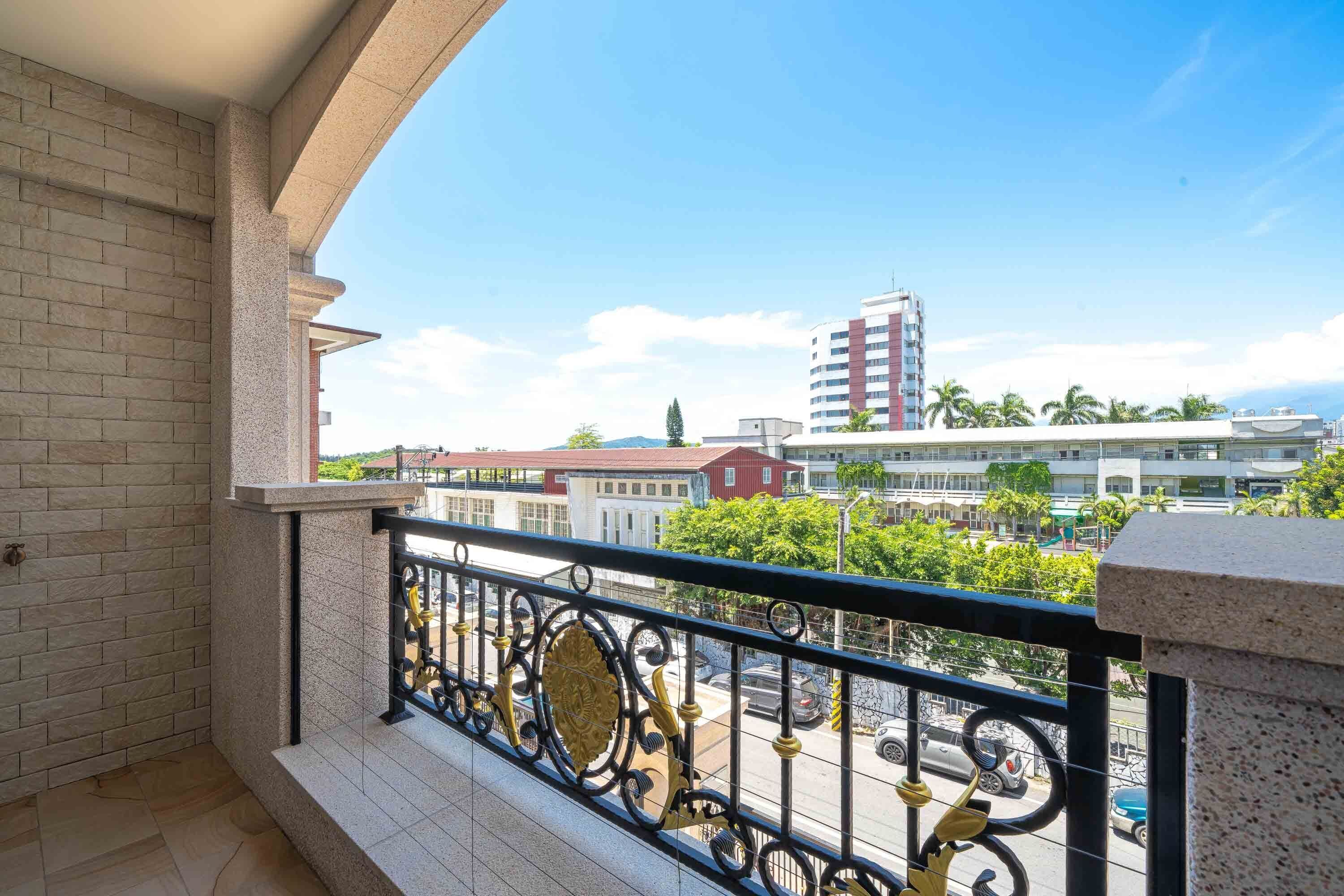 A balcony with a black metal railing and a view of a cityscape with buildings and palm trees.