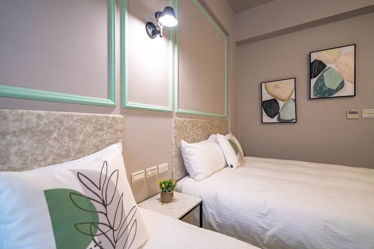 A hotel room with two beds, a small table with a vase of flowers, and wall-mounted artwork.