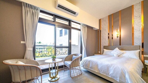 Habitación de hotel con una cama grande, dos sillas, una mesita y un balcón con barandilla.