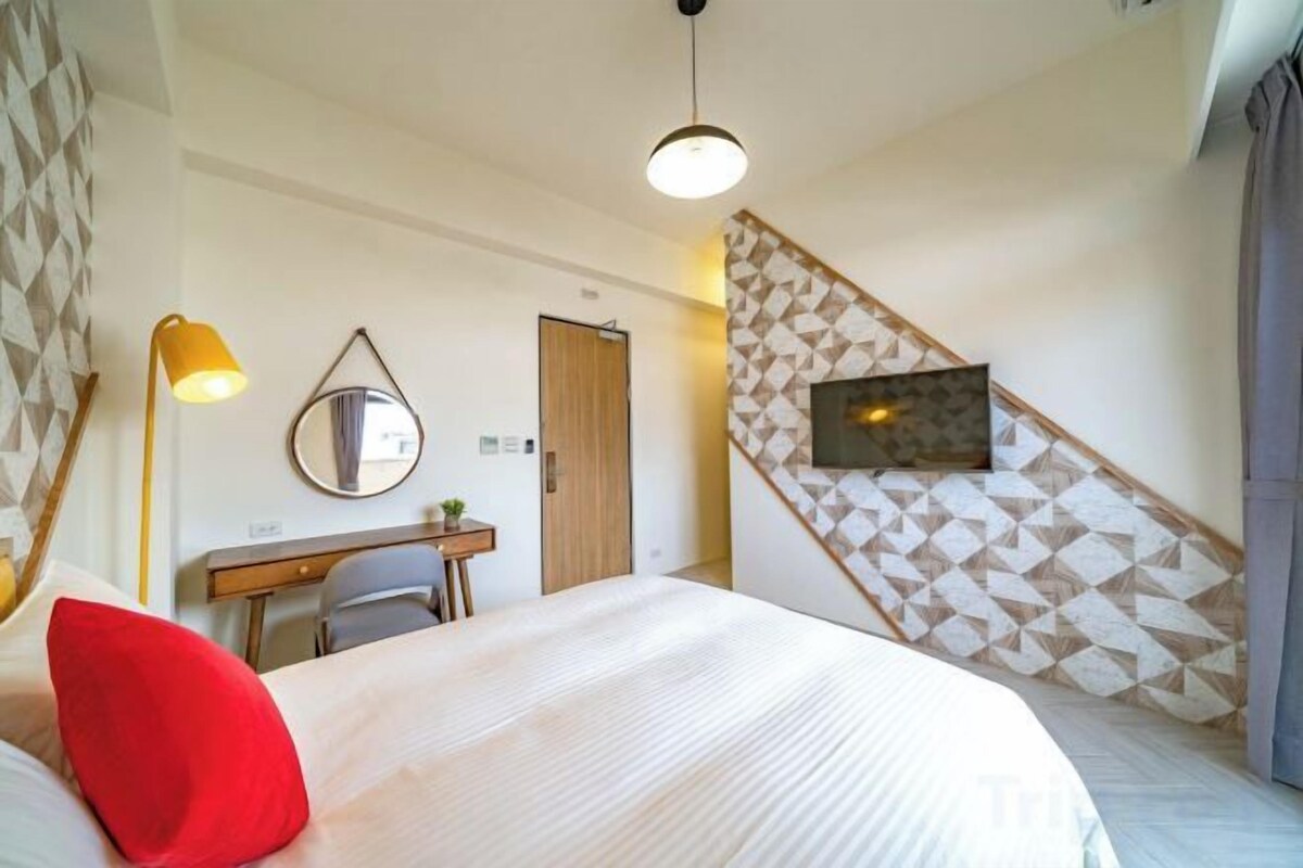 A bedroom with a bed, a desk, a chair, a mirror, and a TV mounted on the wall.