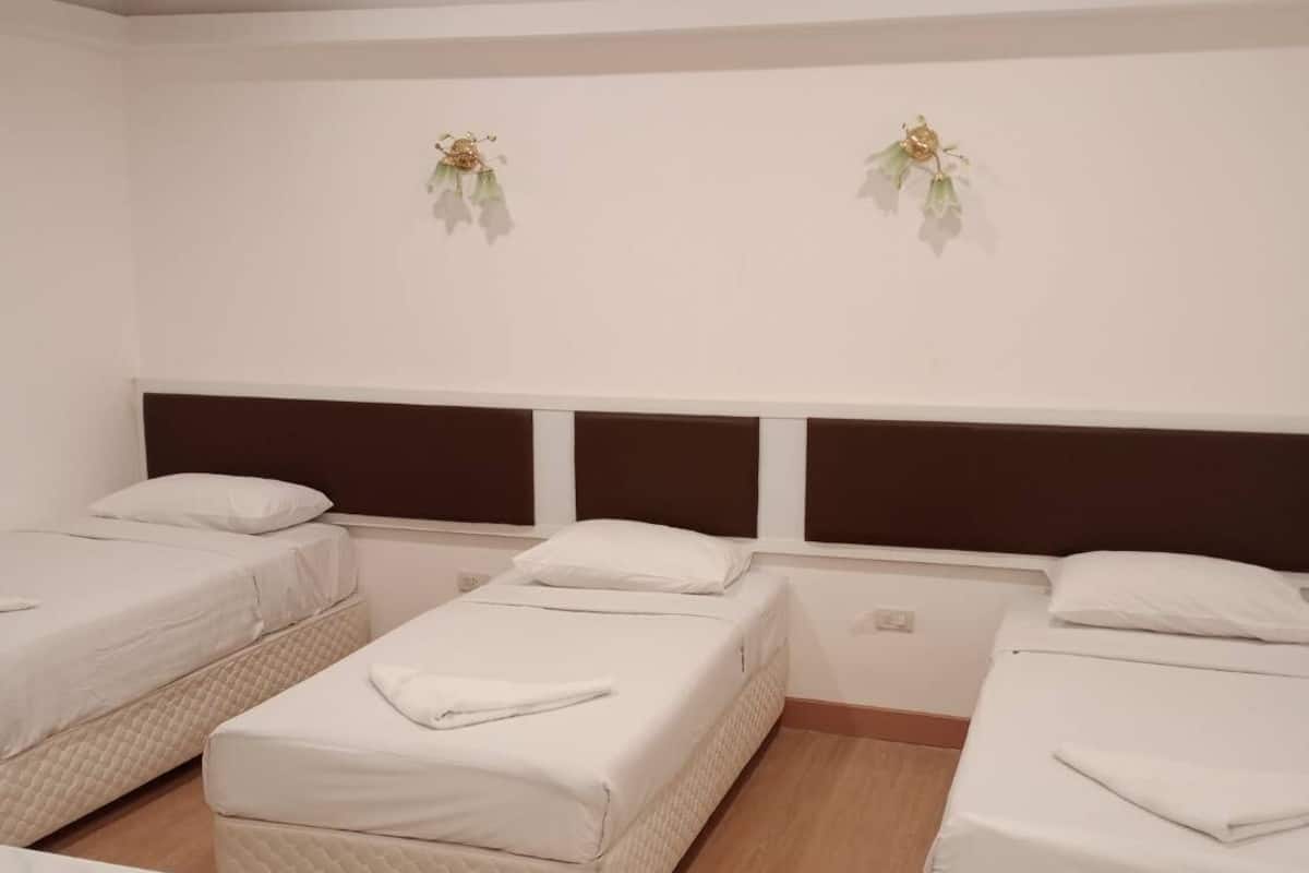 Ein Hotelzimmer mit drei Einzelbetten, Holzboden und einer weißen Wand mit zwei dekorativen Wandteppichen.