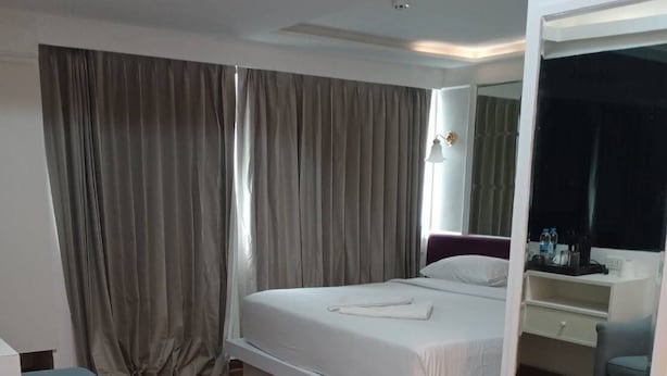 Ein modernes Hotelzimmer mit einem großen Bett, einer Sitzecke mit einem Sessel, einem Nachttisch mit Spiegel und einem Holzboden.